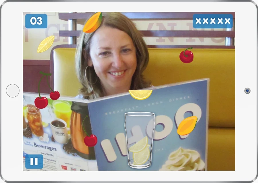 iPad game: lemons, mangoes and cherries fall toward the cup over the camera view of a diner