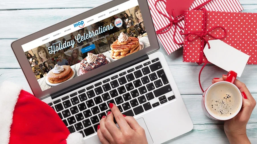 Holiday Celebrations homepage on a laptop surrounded by gifts and a mug of cocoa