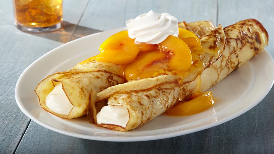 Crepes filled with cream and topped with peaches and whipped cream