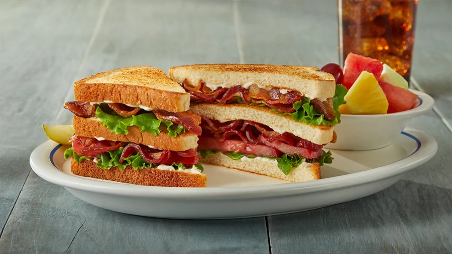 Triple-decker BLT sandwich with a side of fresh fruit